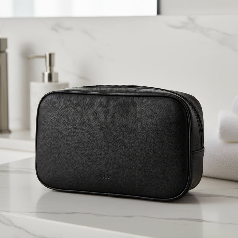 Black toiletry bag on a bathroom counter with a sink and towels in the background